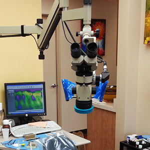 Dental operating microscope setup in a treatment room with a desktop monitor displaying digital scans.
